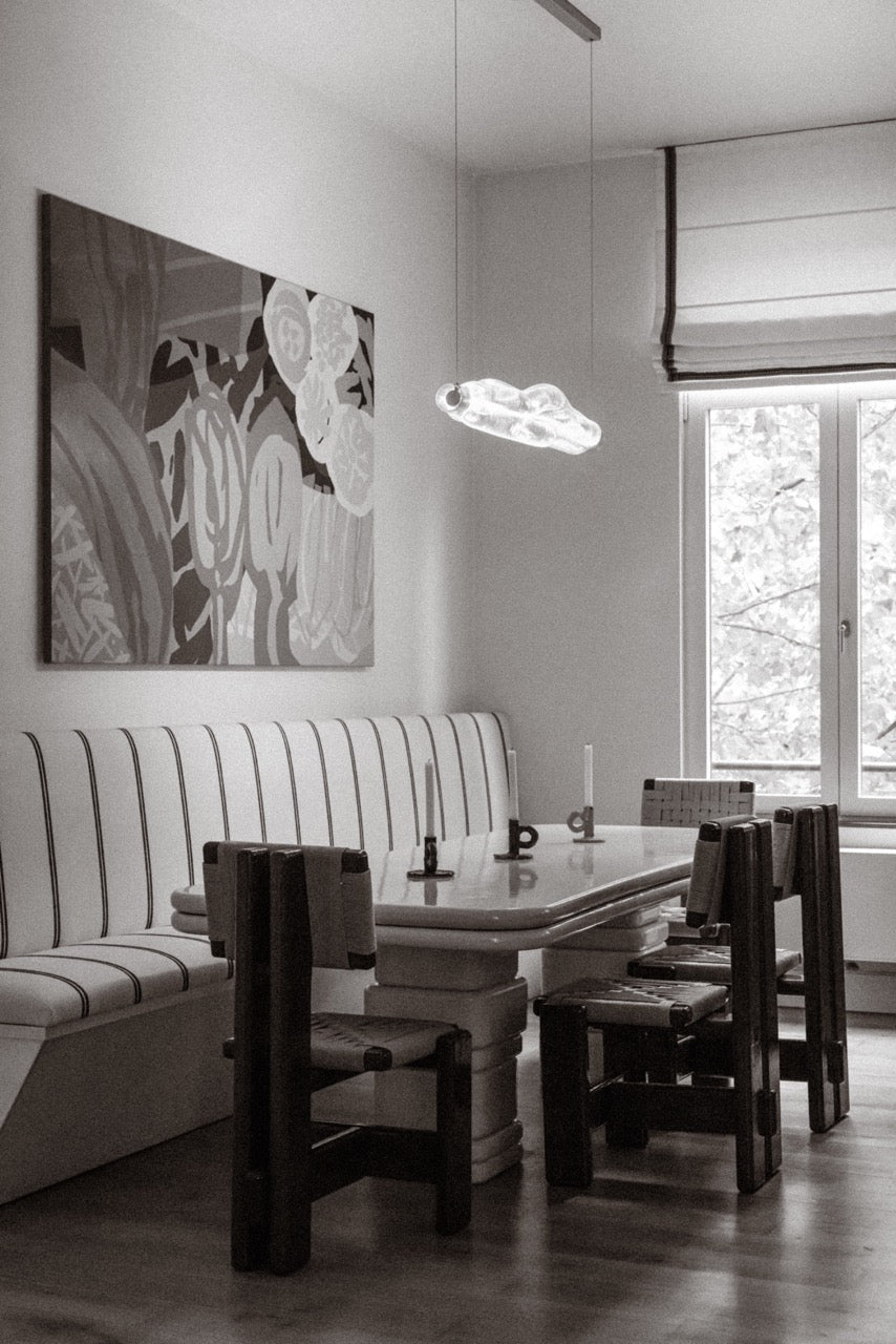 Dining room with a table, Bemelmans chairs, and a bench against a wall with abstract art.